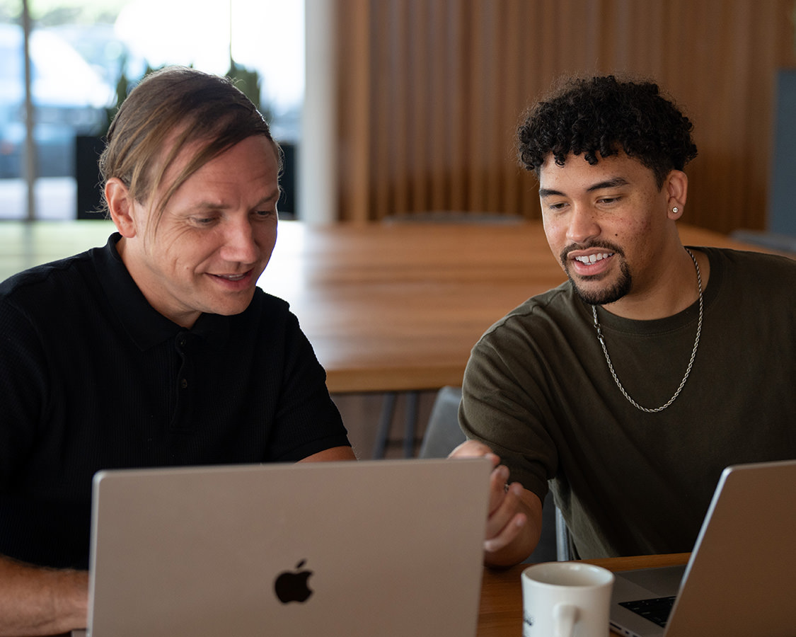 Two men smiling and working on a laptop together.