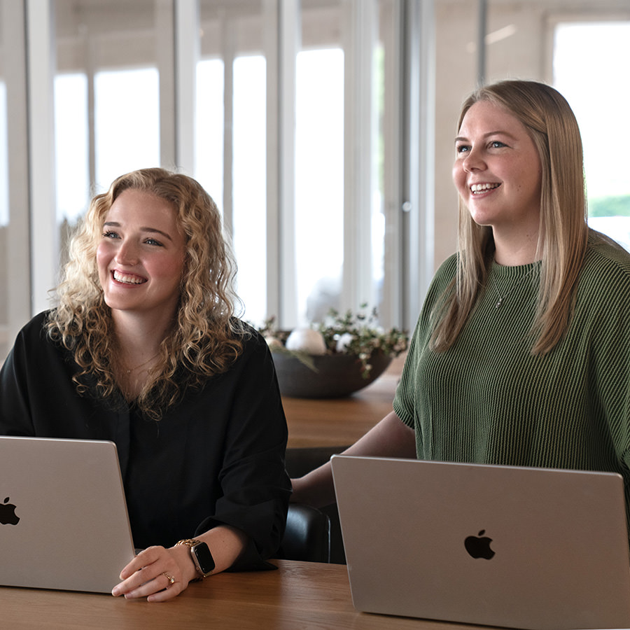Two women smiling and working on laptops.