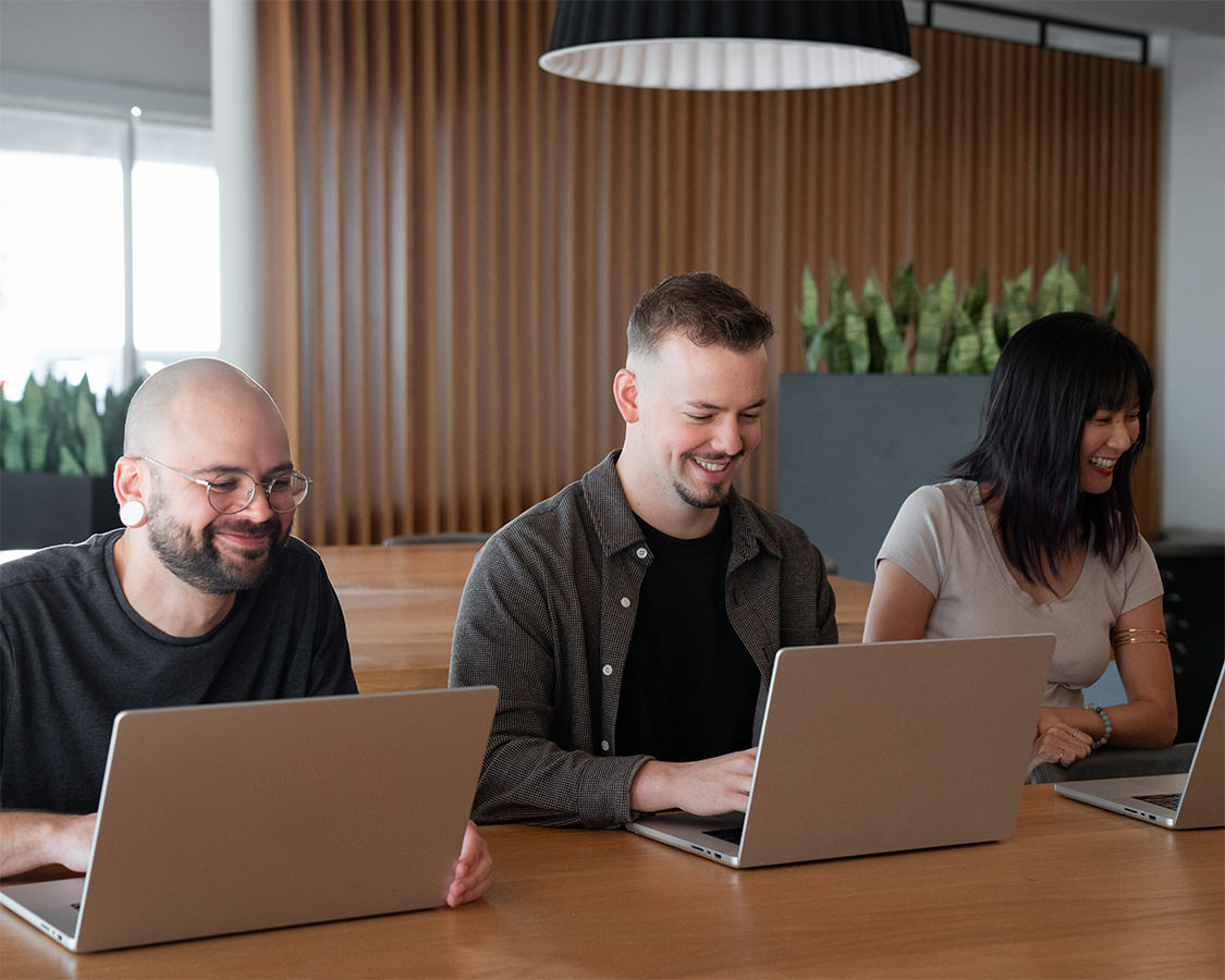 Two men and a woman smiling while working on laptops.