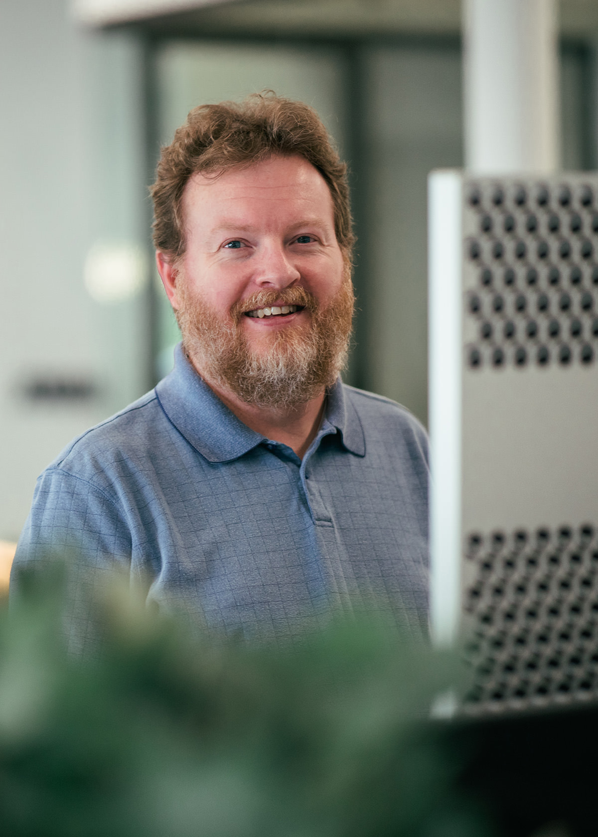 A handsome ginger smiles at the camera while working on a desktop computer.