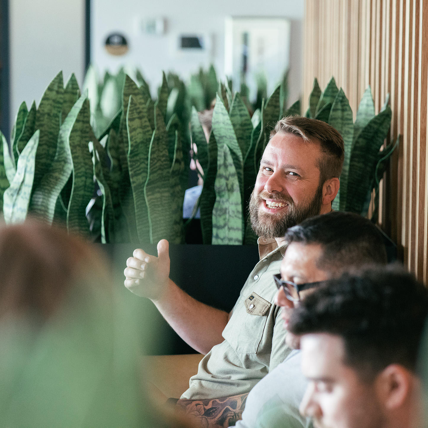 A bearded Texan sitting in a work lounge smiling at his compadres.