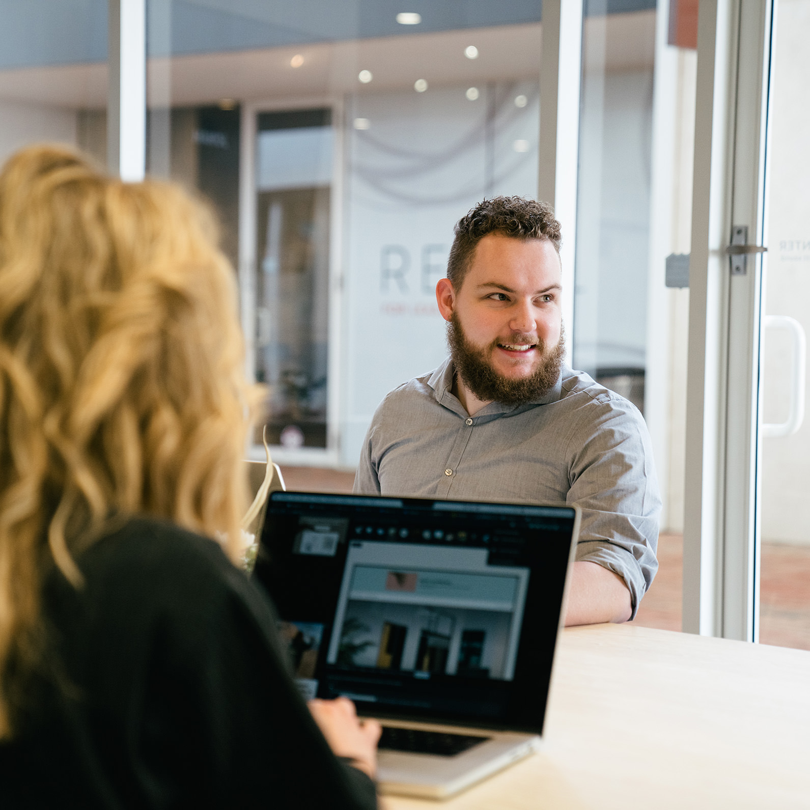 A young professional man smiling with a window behind him in an office.