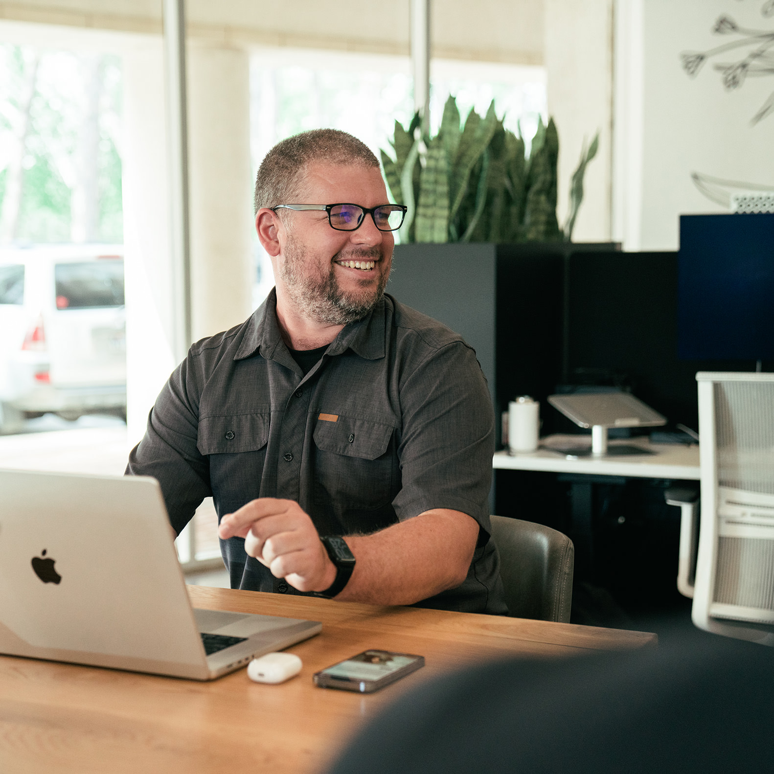A talented developer sitting at a table working on a laptop computer and smiling off into the distance.