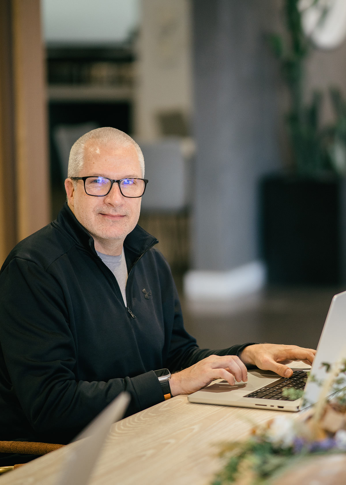 A gray-headed man sits at a conference table working on a laptop.