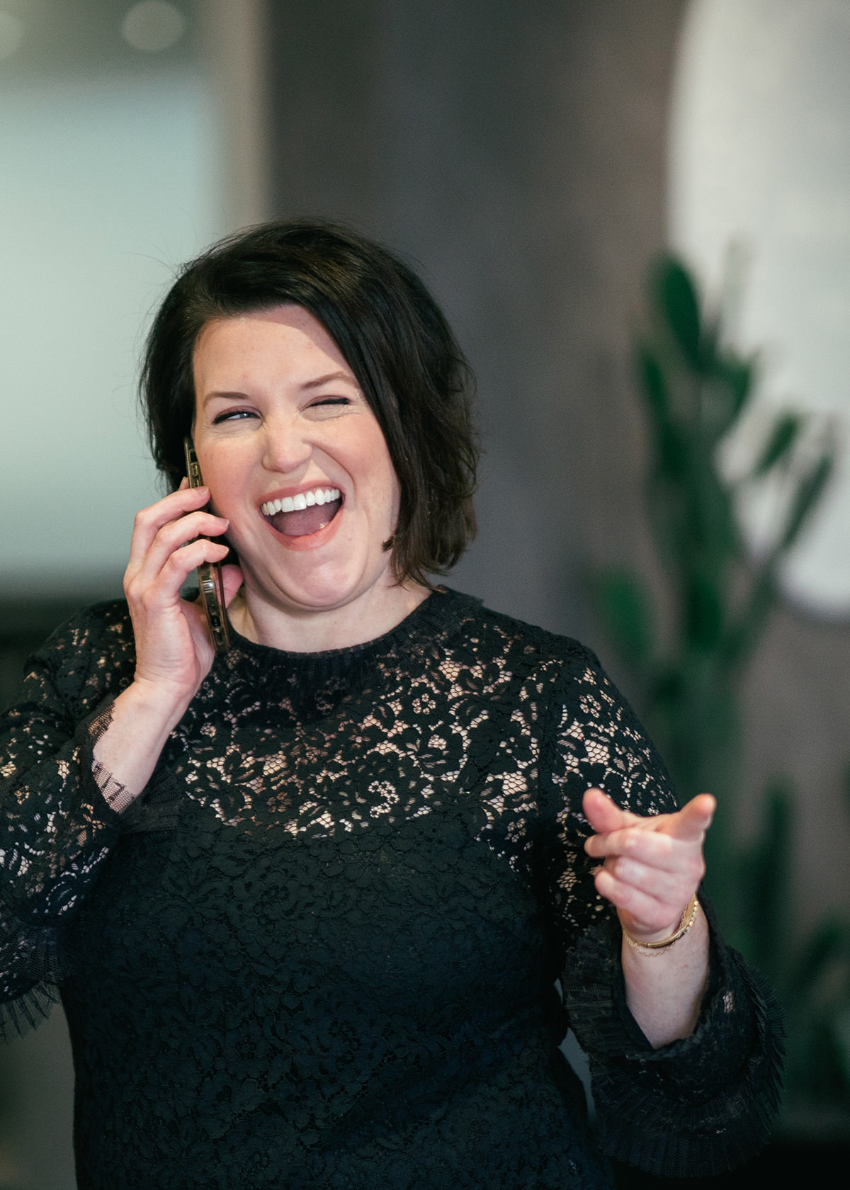 A woman talks on a phone while pointing and winking at some fine young man across the way.
