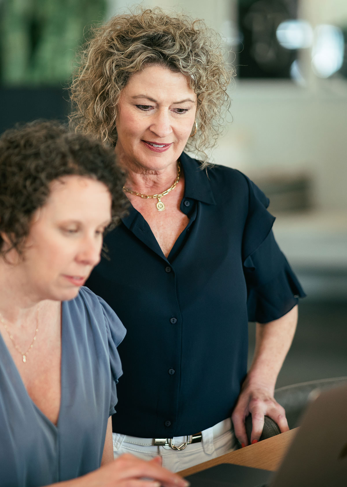 Two women working together in an open office while looking at a laptop computer.