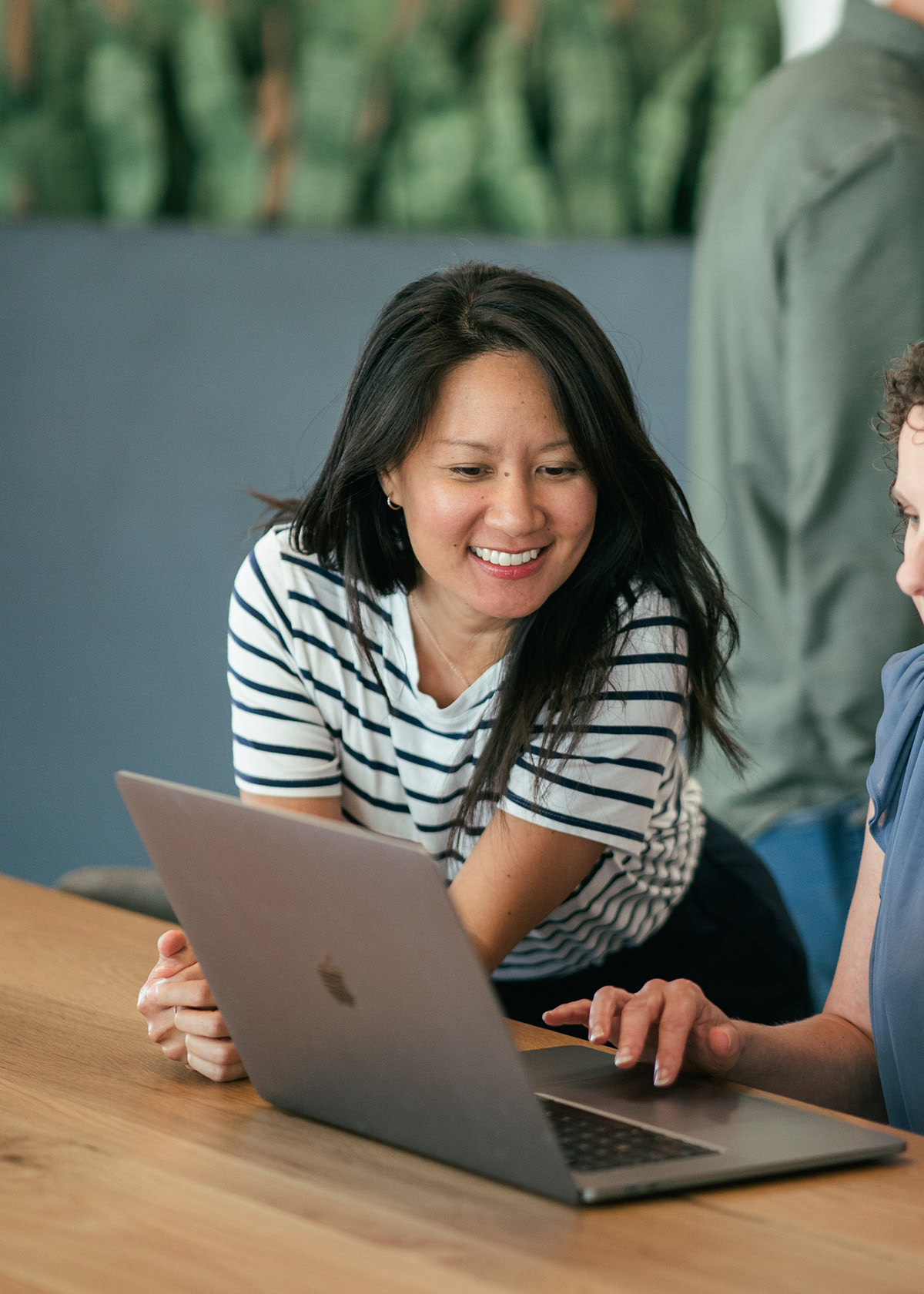 A woman leaning on a table looking at a laptop computer with another woman.