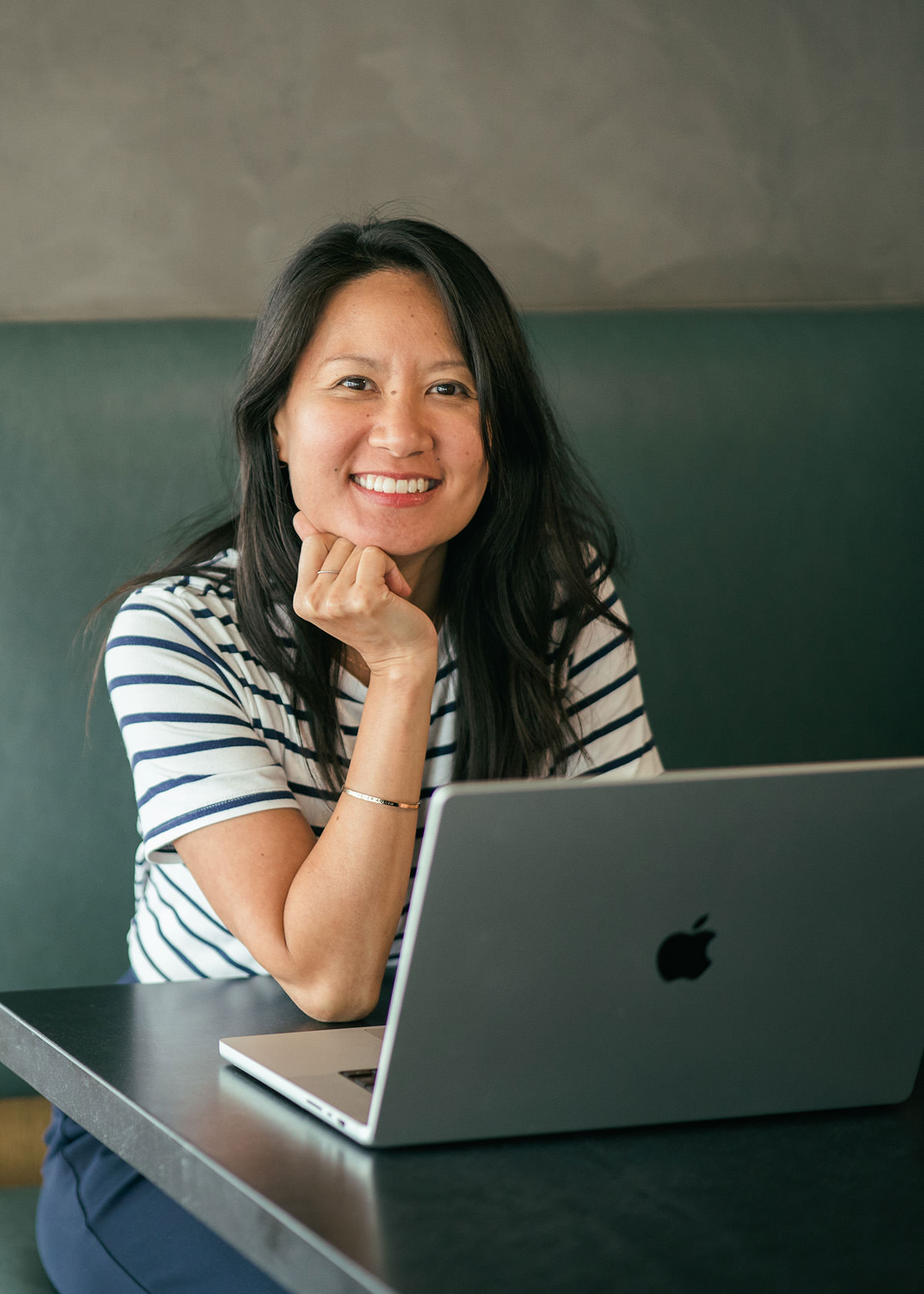 A young woman working at a table with a laptop in front of her.
