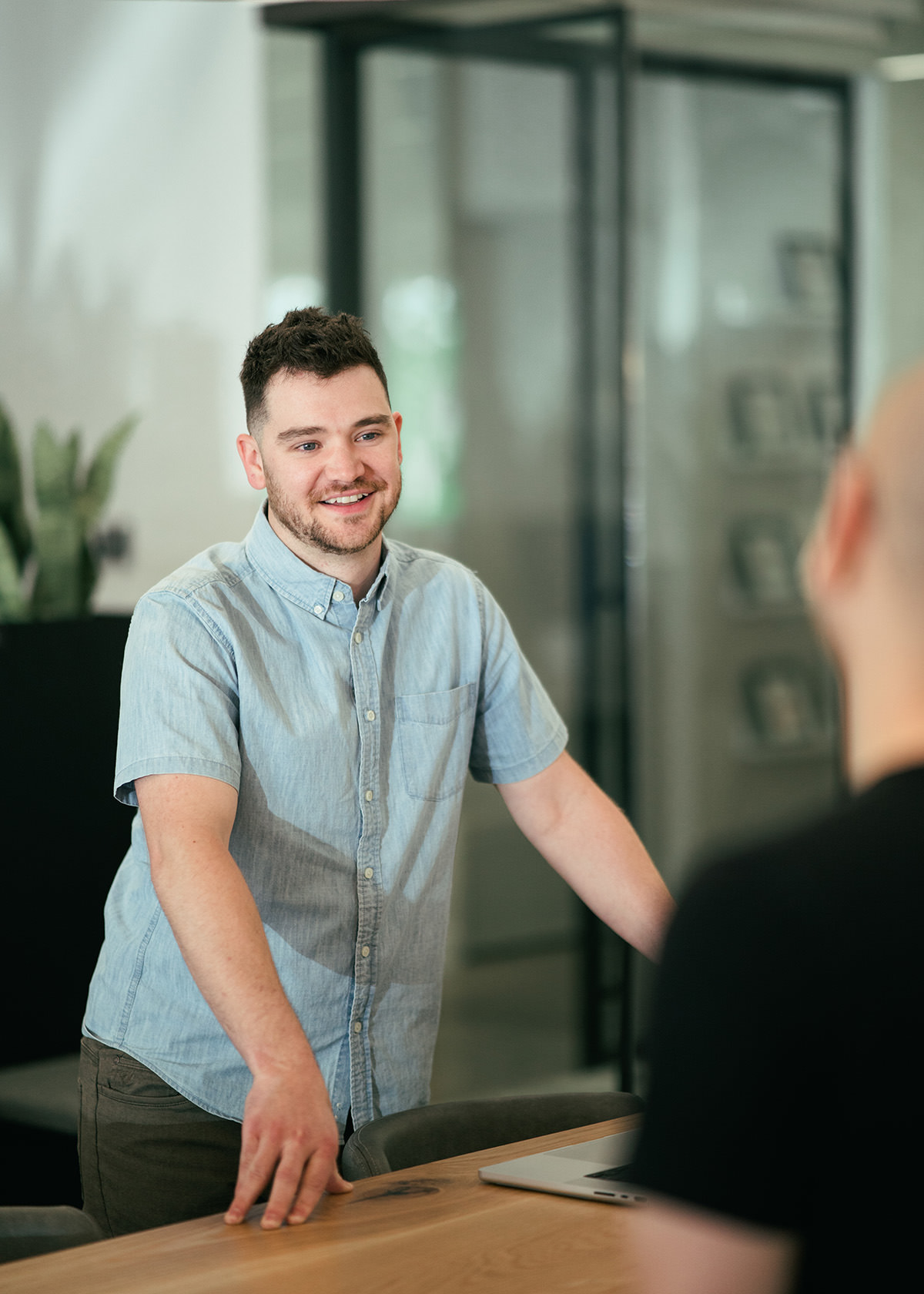 A young professional talking to another person while standing on opposite sides of a table.