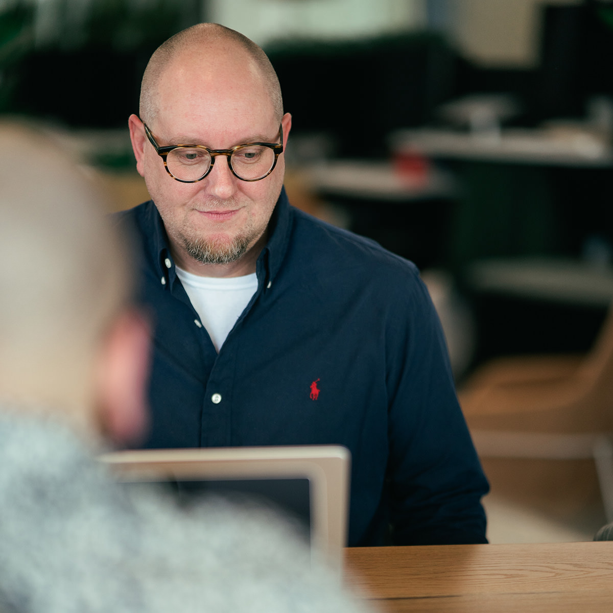 Two bald men sitting at a table working on their laptop computers.