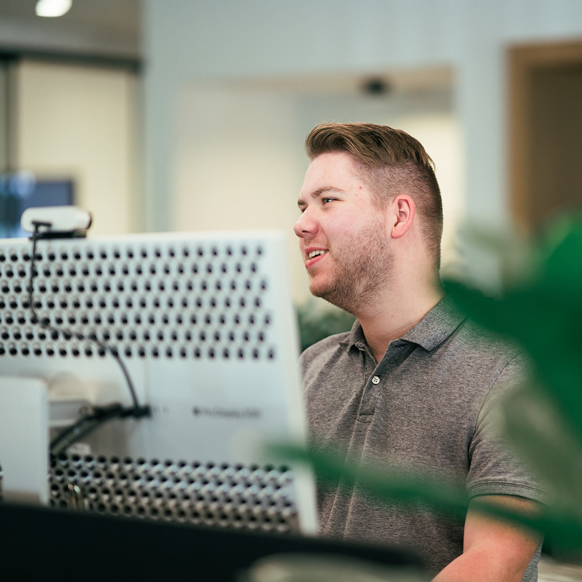 A man standing at a desk working while smiling at someone off in the distance.