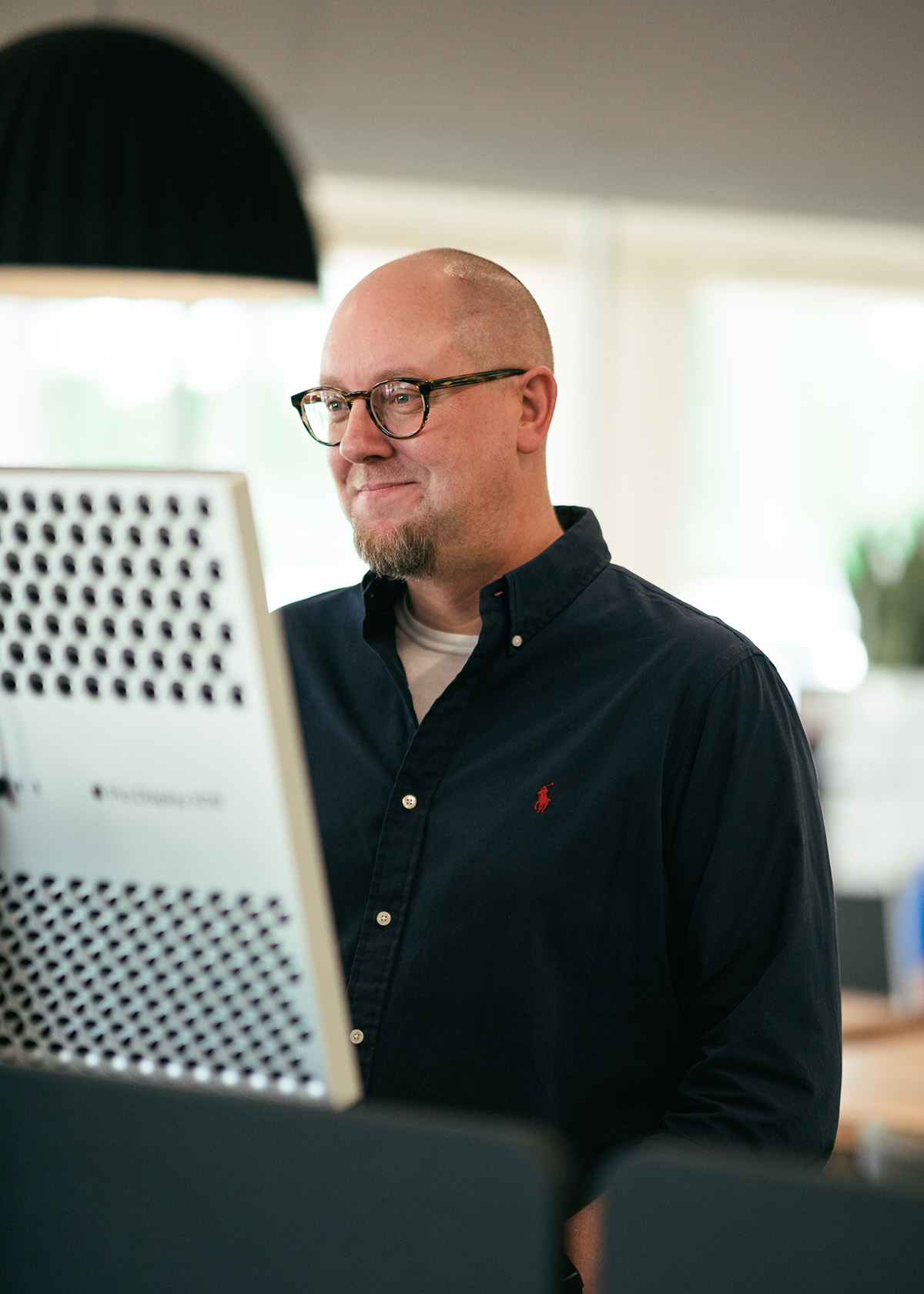 A middle-aged bald man standing up and working in an open office area.