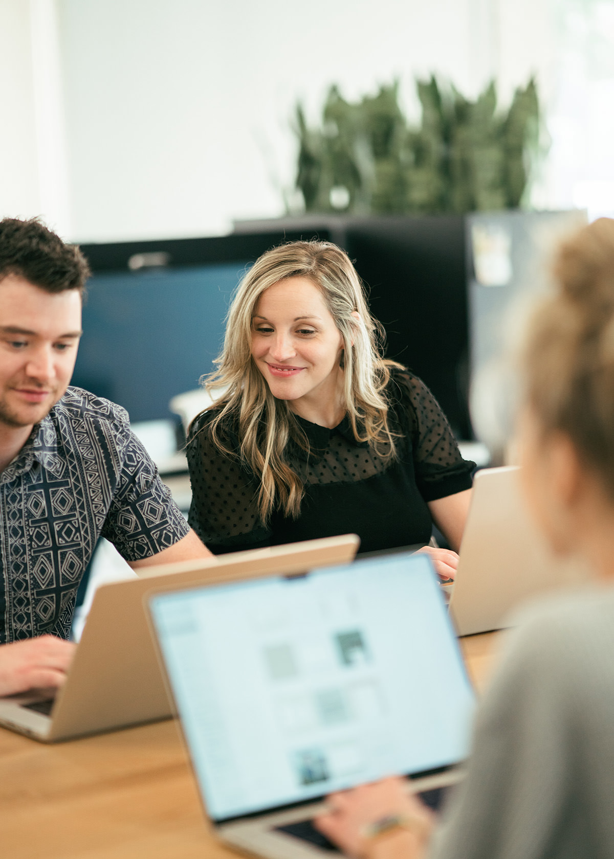 Several young people sitting in a modern office area looking at laptop computers and smiling.