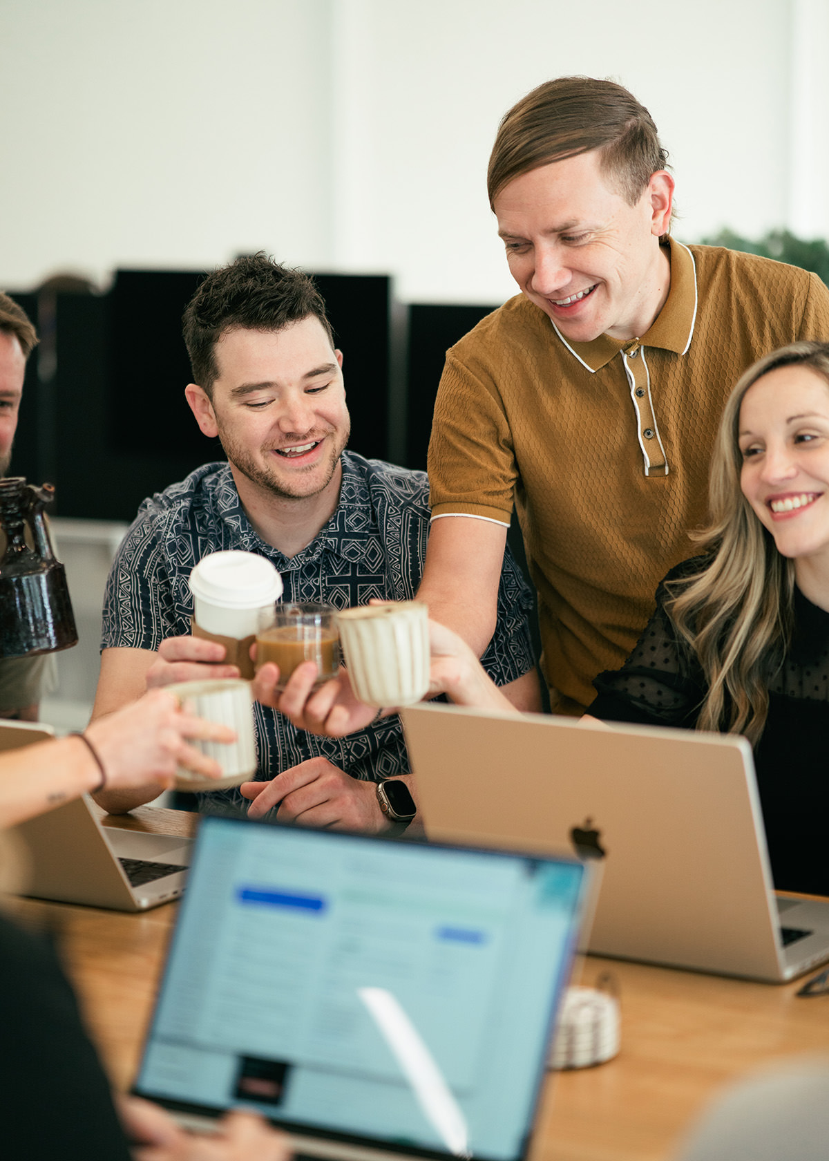 Several people sitting at a table putting their coffee cups together and smiling.