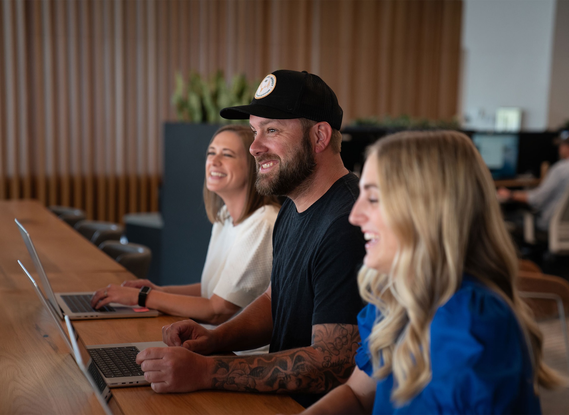 Two women and a man laughing while they work on laptops.