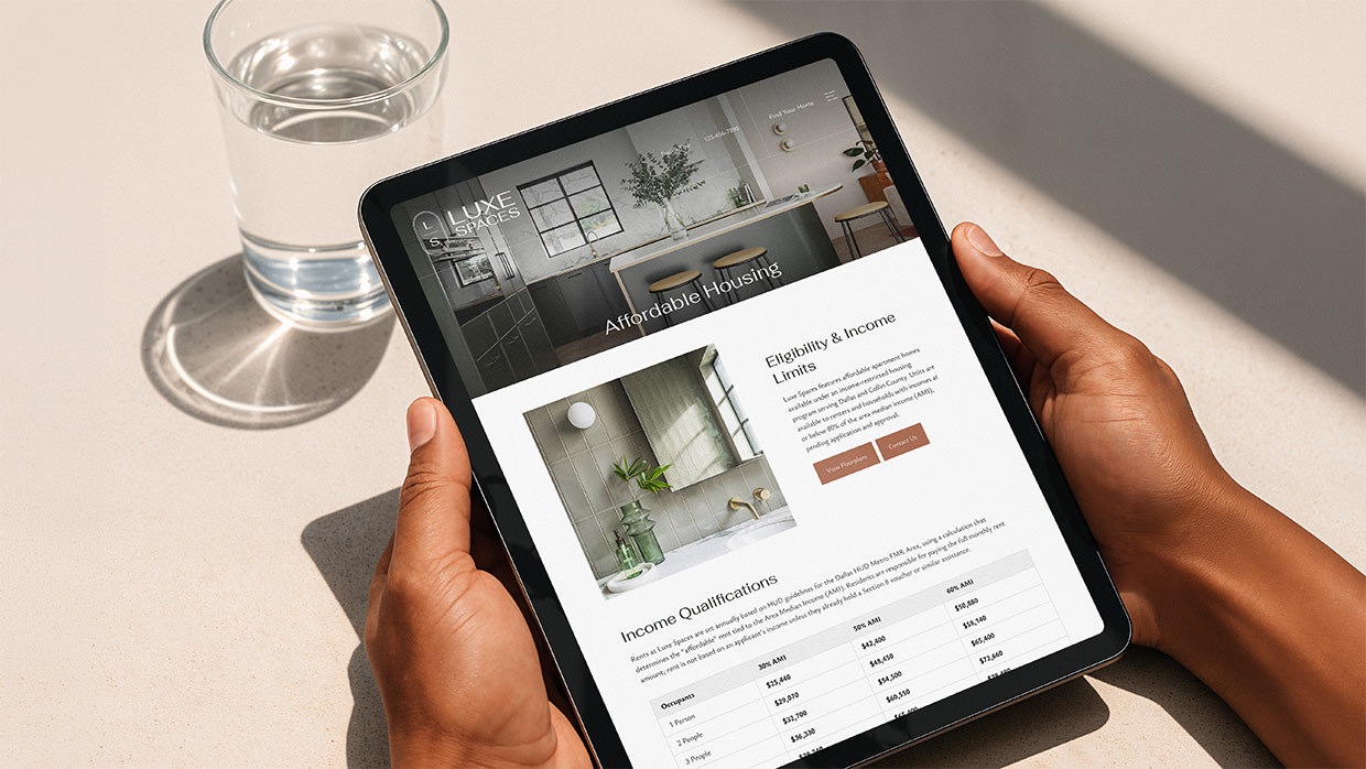 Hands holding a tablet with Luxe Spaces Affordable Apartments website.