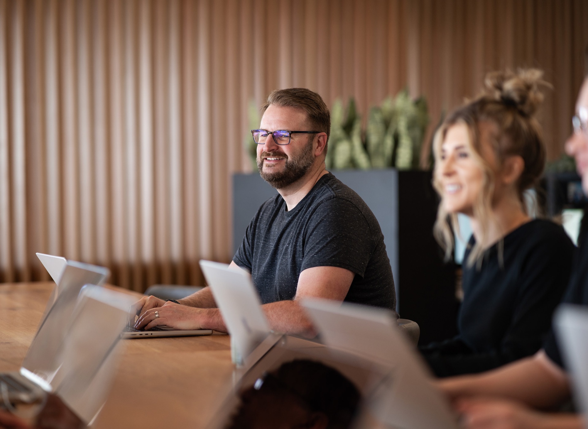 A man and woman smiling while working on laptops.