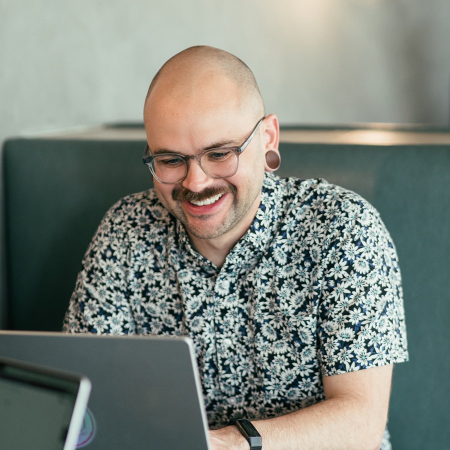 A good-looking bald man with a mustache working on a laptop computer.