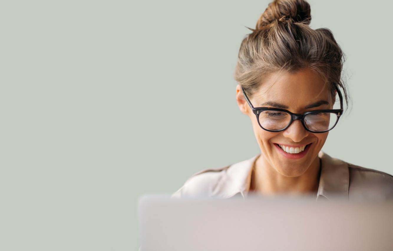 A woman with glasses sitting in front of a computer and smiling.