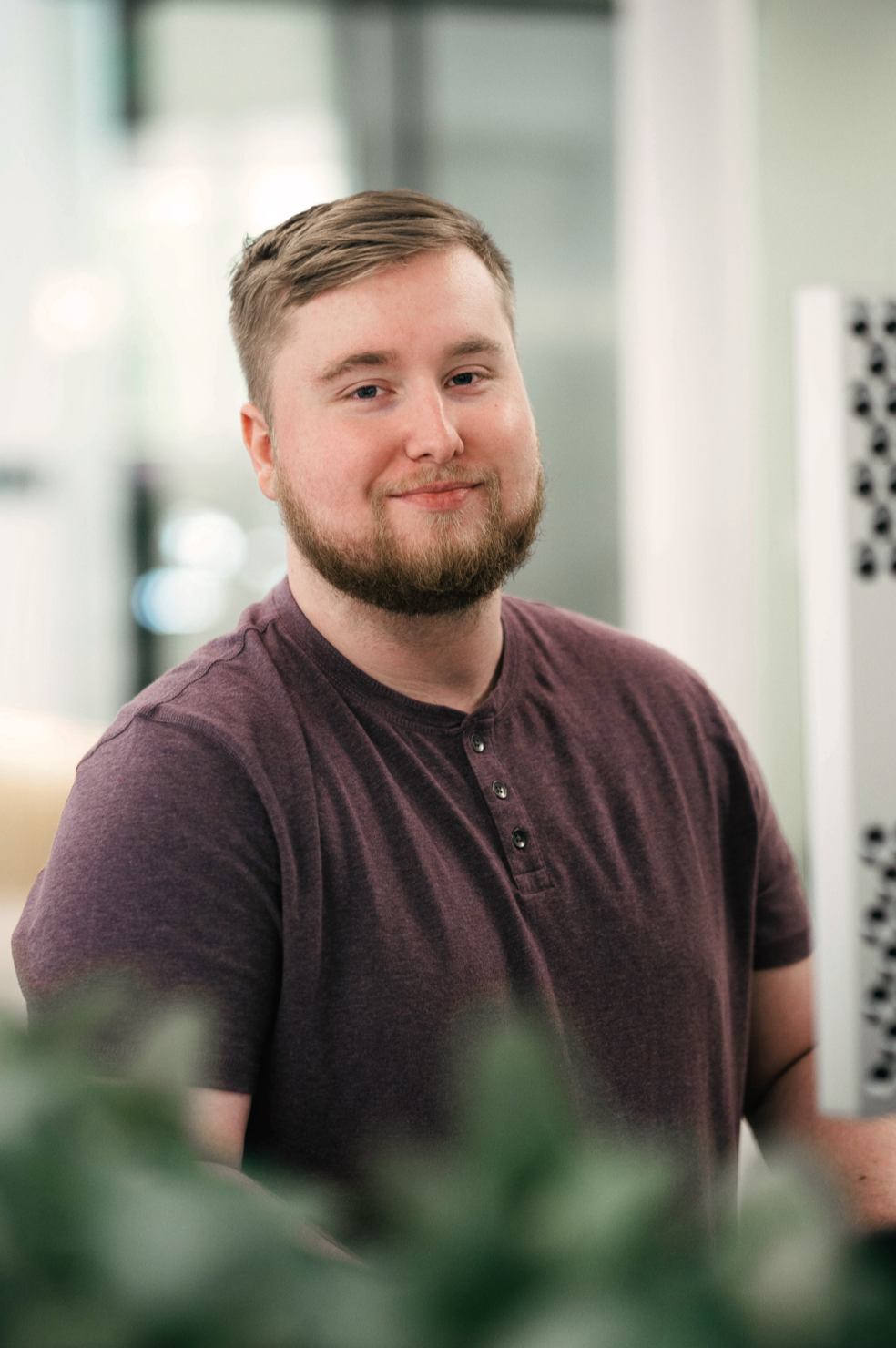 A young man standing up and working in an open office area.