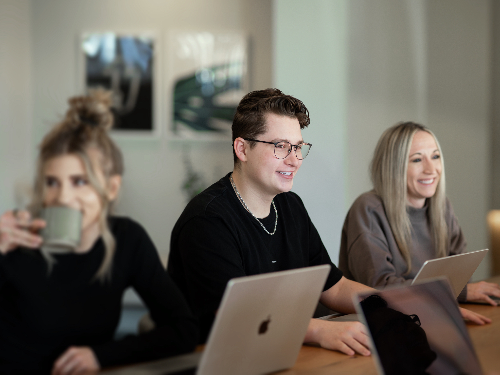 Several young people sitting in a modern office area looking at laptop computers and smiling.