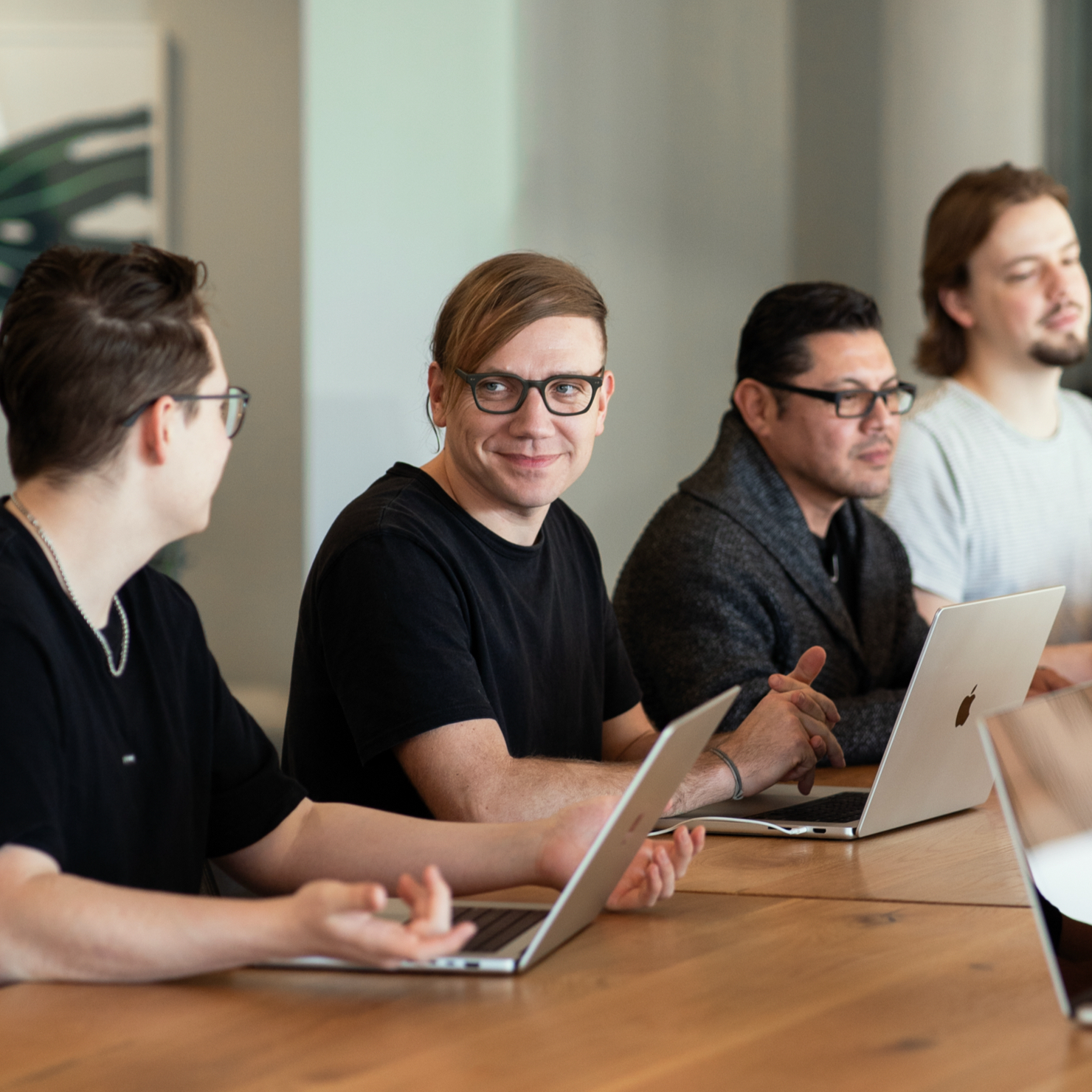 A man sitting at a table with a laptop in front of him and talking to someone at the table.
